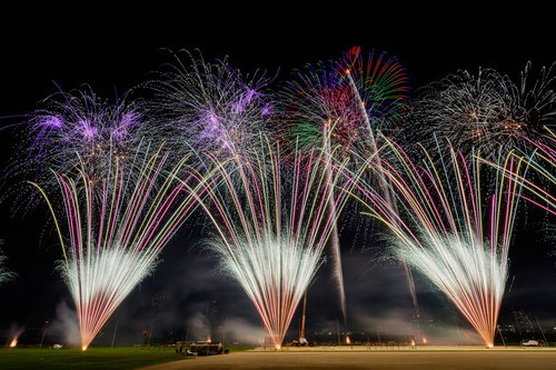 夜空に扇状に噴き上げる打上花火の光跡が放射状に広がる様子