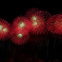 夜空に流れる赤い打上花火とスターマインの爆発の写真