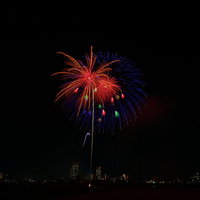 夜空に小さく弾ける赤と青の打ち上げ花火の光跡の写真
