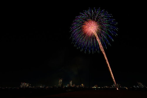 都会の夜空に打ち上がる花火と光の軌跡、スターマインが彩る夜景