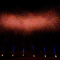 夜空に炸裂する赤いスターマインの光跡と発光点の写真