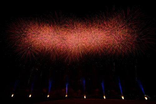 夜空に炸裂する赤いスターマインの光跡と発光点