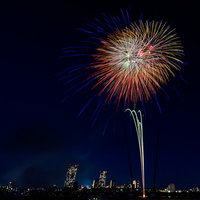 都会のビル群と夜空に打ち上がる花火と光の競演の写真