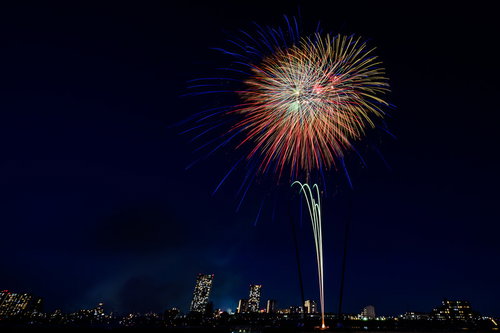 都会のビル群と夜空に打ち上がる花火と光の競演