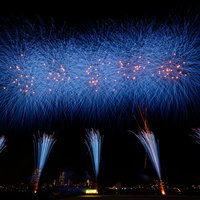 夜空に青く炸裂するスターマインと打上花火の写真