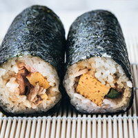 コンビニで買った恵方巻、竹のすだれの上に2本並べた食卓の写真