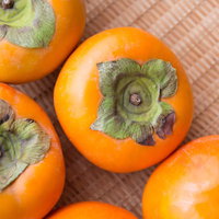 ざるに入った秋の柿、新鮮な収穫果実、旬の農産物の写真