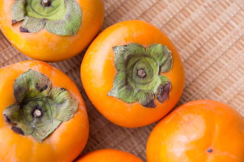 ざるに入った秋の柿、新鮮な収穫果実、旬の農産物の写真