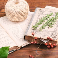 レシピが書かれた洋書の上に並べられた薬草と麻縄の写真