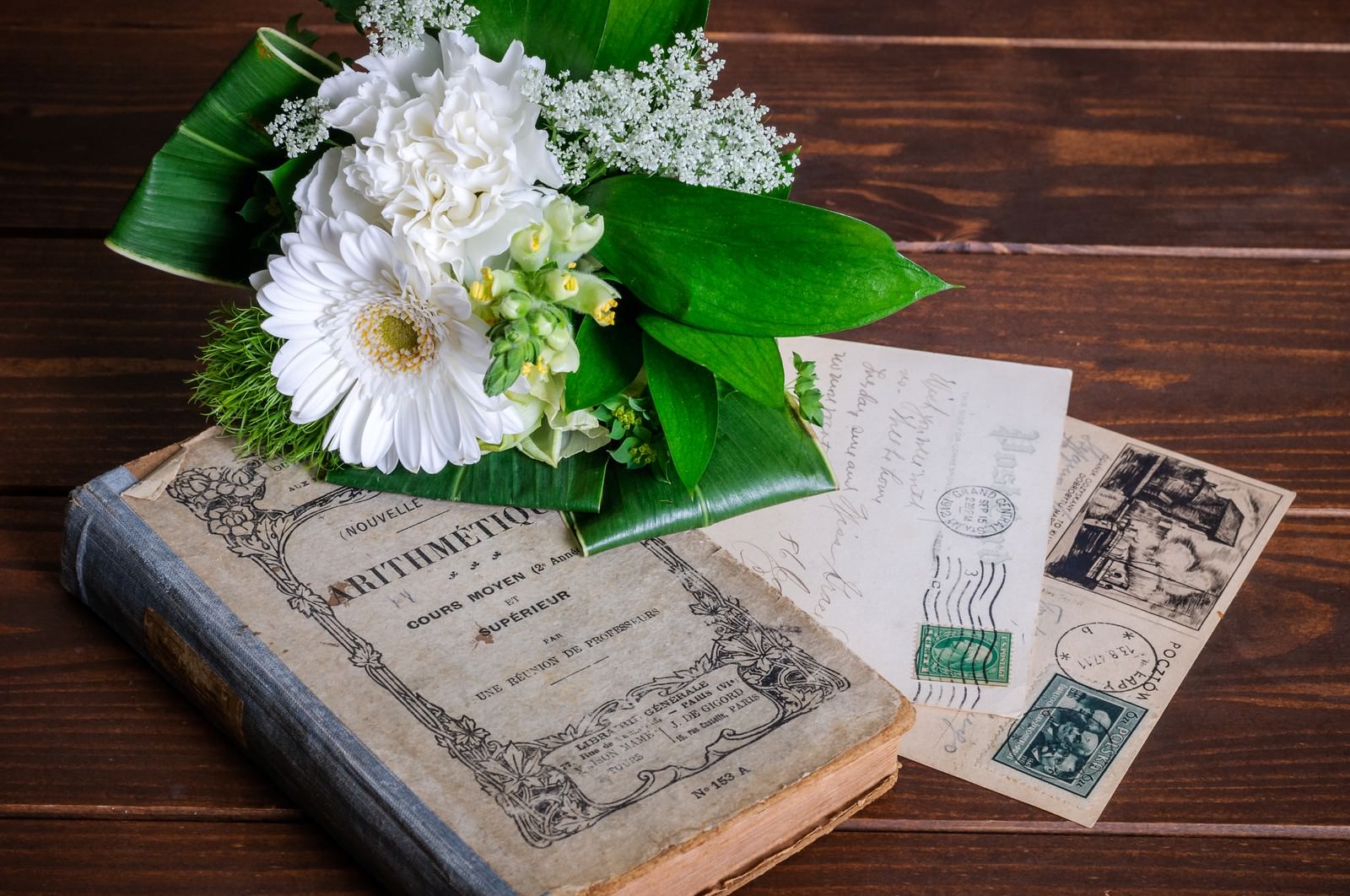 木製テーブルの上で古い洋書と葉書の上に置かれた白い花のブーケ