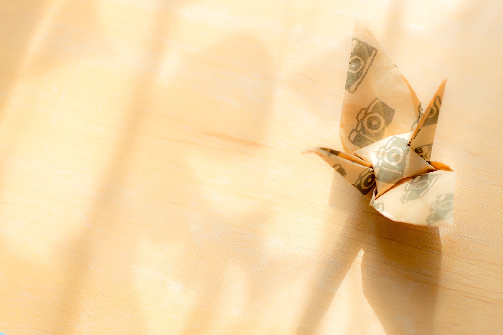 暖かい光が射し込む中に置かれたカメラ柄の折り紙で作られた鶴