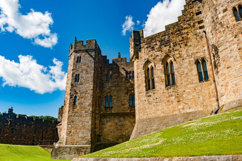 青空の下に建つアニック城の石造りの外観と緑の芝生