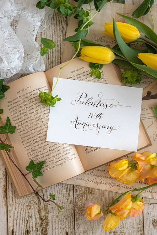 洋書に添えた白いアニバーサリーカード、黄色い花とメッセージ