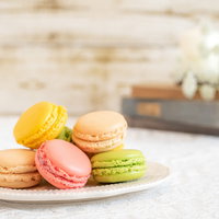 白い皿に並ぶカラフルな洋菓子マカロン、黄色とピンクの焼き菓子の写真