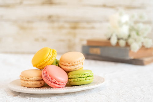 白い皿に並ぶカラフルな洋菓子マカロン、黄色とピンクの焼き菓子
