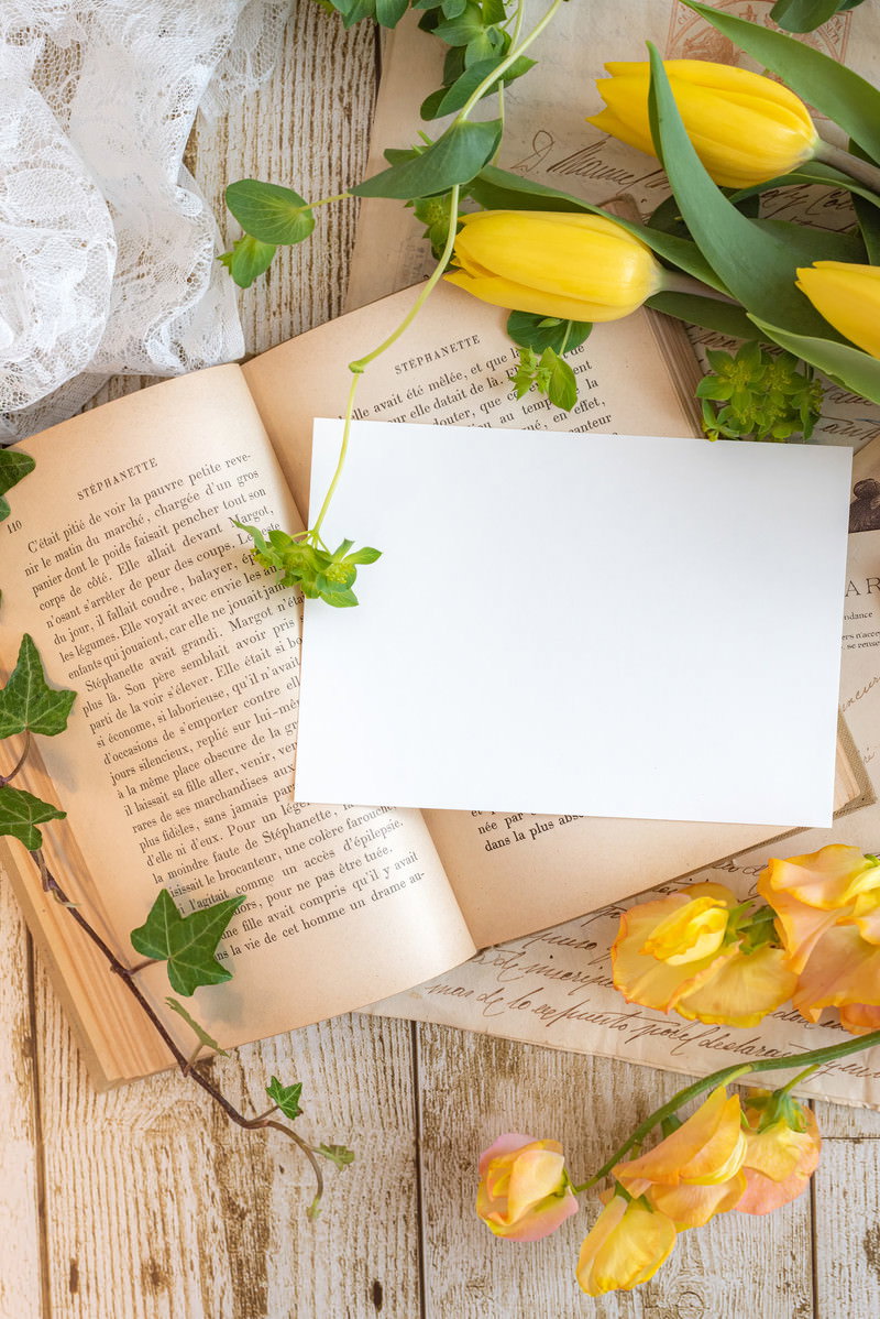 木目テーブルの上に開かれた洋書とその上の白いハガキ、レモンと植物