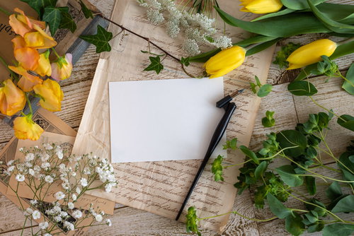 机の上に置かれた黄色い花と万年筆、洋書、白い紙
