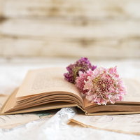 木目テーブルに置かれた開いた洋書と花のしおりの写真