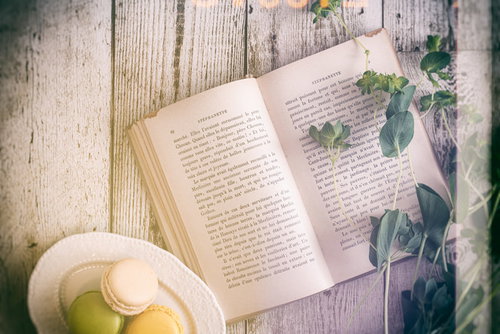 木製テーブルに置かれた洋書とクリーム色のマカロンの読書風景