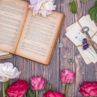 ピンクのバラと白い生花に囲まれた古書と手紙の写真