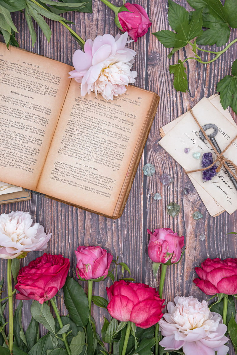 開かれた古書と手紙を囲むピンクのバラと白い生花