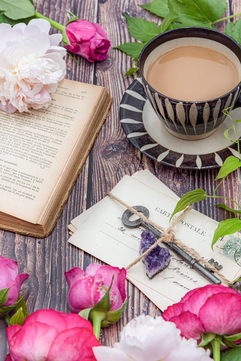 古書とコーヒーカップが置かれたテーブルにピンクのバラの花びらが散る