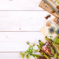 白い木目の背景に散らばった古書と手紙、ピンクの花の雑貨の写真