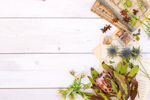 白い木目の背景に散らばった古書と手紙、ピンクの花の雑貨