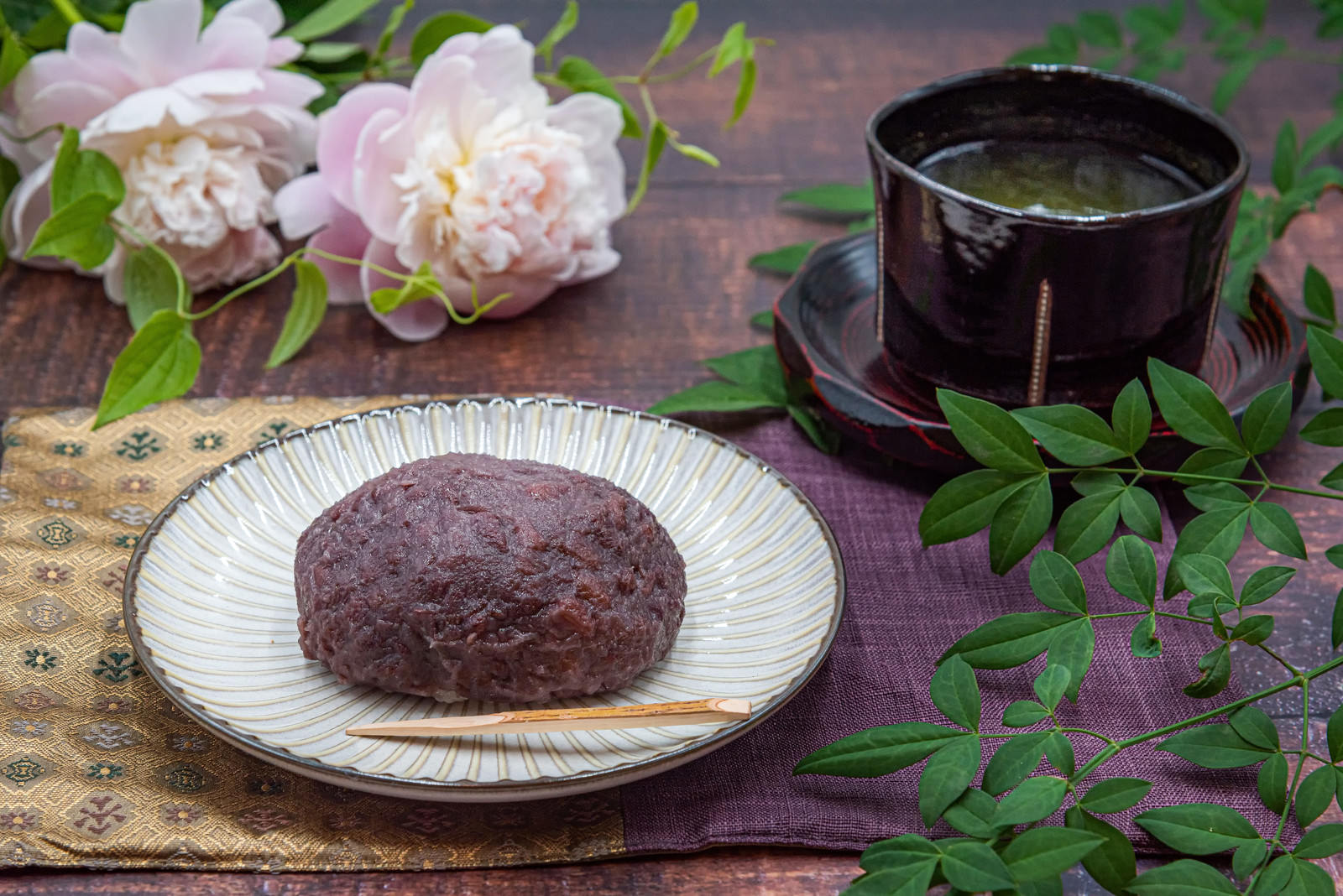 白いお皿に盛られた茶色いおはぎと黒いお茶碗が木のテーブルに置かれている