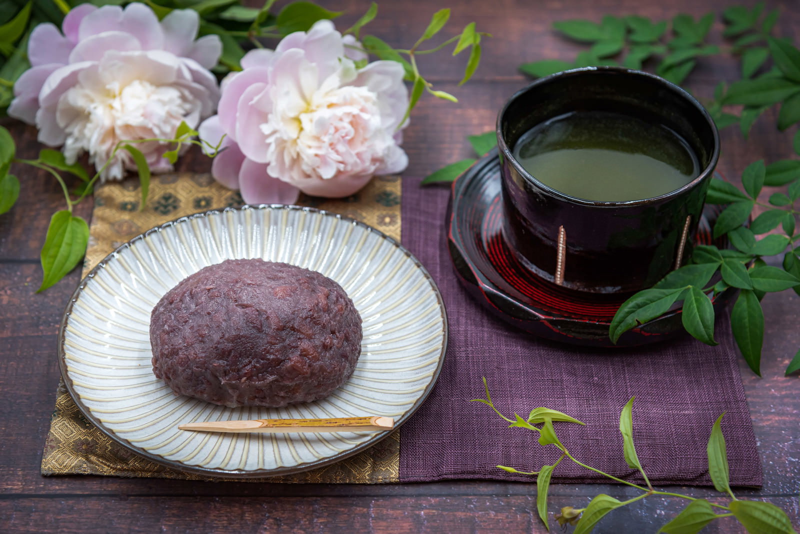 木製トレイに置かれたおはぎと緑茶、背景に薄紫の牡丹