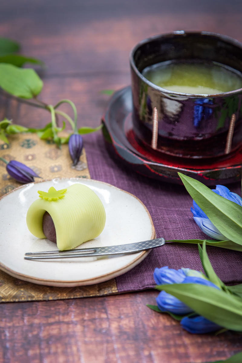 白い皿に盛られた練り切りと緑茶が入った茶碗、紫の花が添えられたティータイムの様子