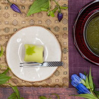 白い皿に盛られた緑色の練り切りと抹茶のお茶を俯瞰で配置の写真