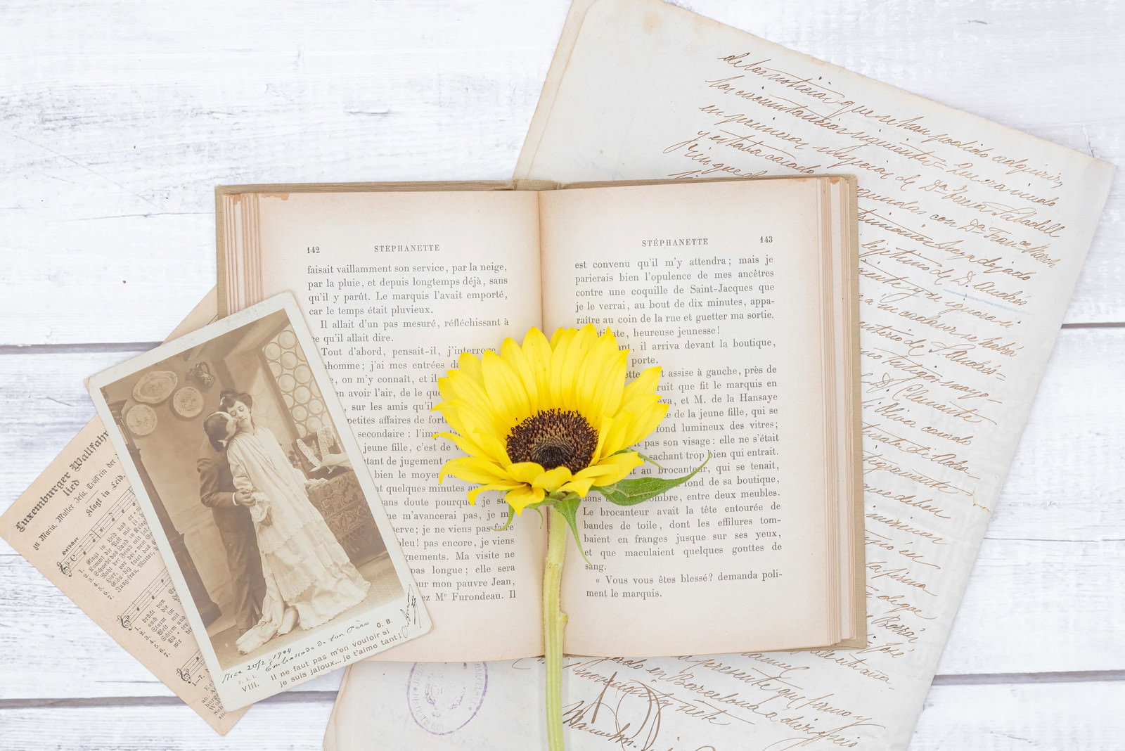 白い木目背景に開いた古い洋書と黄色い向日葵、アンティークな手紙が配置された写真