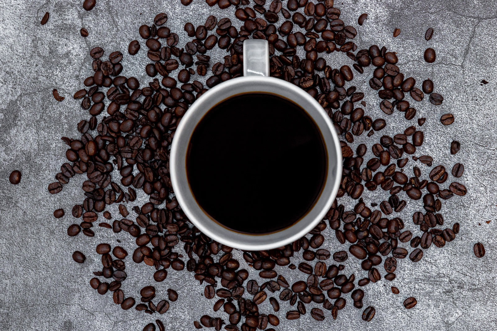 白いコーヒーカップとその周りに散らばるコーヒー豆