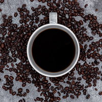 白いコーヒーカップの周りを囲うコーヒー豆の写真
