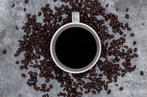 白いコーヒーカップの周りを囲うコーヒー豆