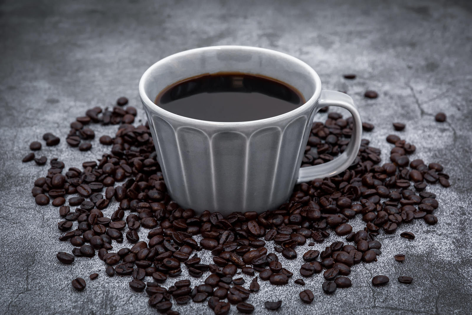グレーの縞模様のコーヒーカップとブラックコーヒー、周囲に散らばるコーヒー豆
