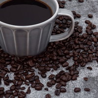 グレーのカップに入ったコーヒーとばら撒かれたコーヒー豆の写真