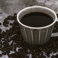 白いカップに注がれたブラックコーヒーと散らばる珈琲豆の写真