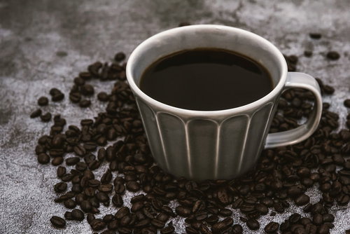 白いカップに注がれたブラックコーヒーと散らばる珈琲豆
