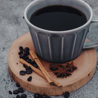 木製コースターに置かれた珈琲とシナモンスティックの写真