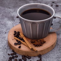 散らばったコーヒー豆とシナモン、木製コースターの珈琲の写真