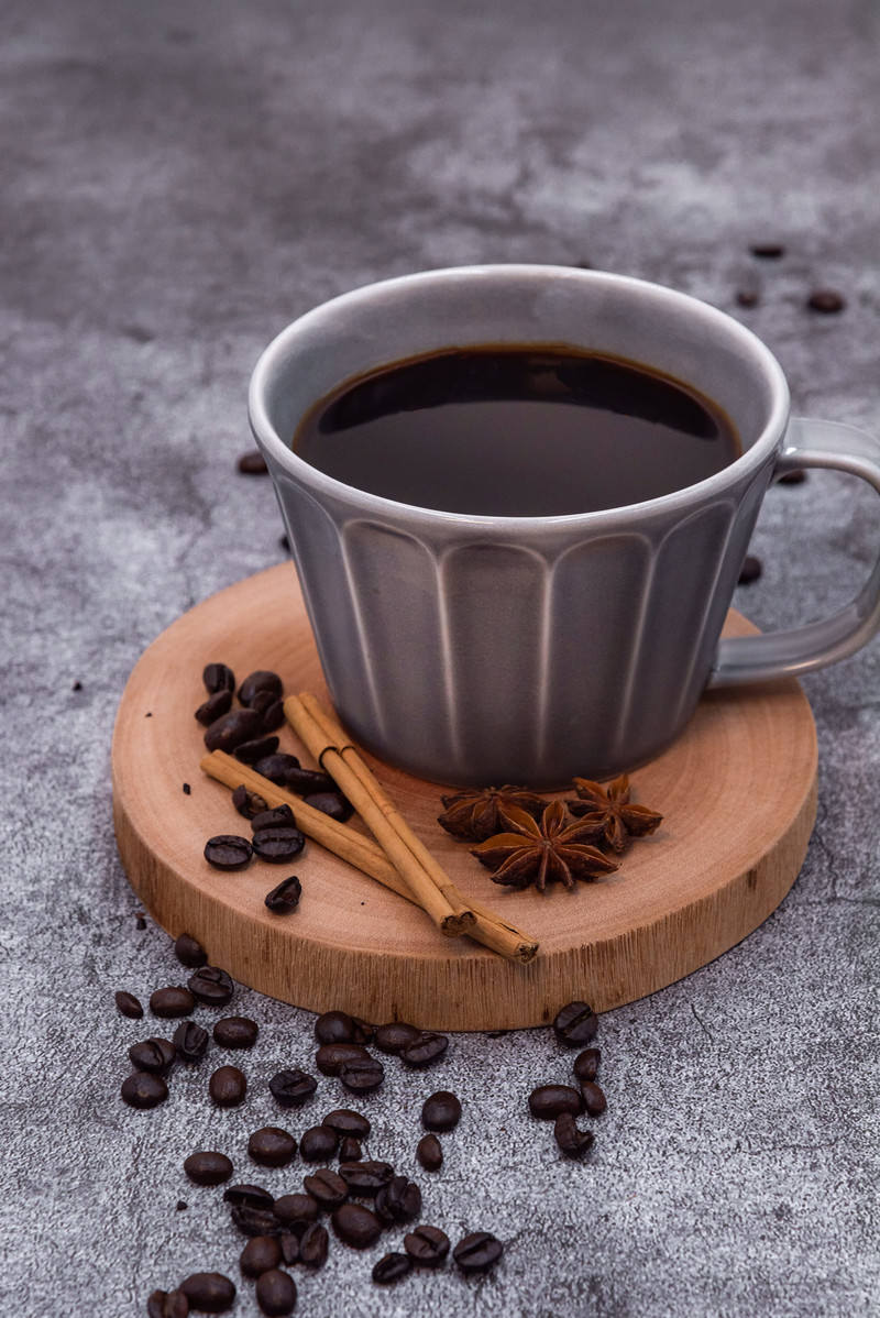 木製コースターに置かれたコーヒーカップとコーヒー豆、シナモンスティック