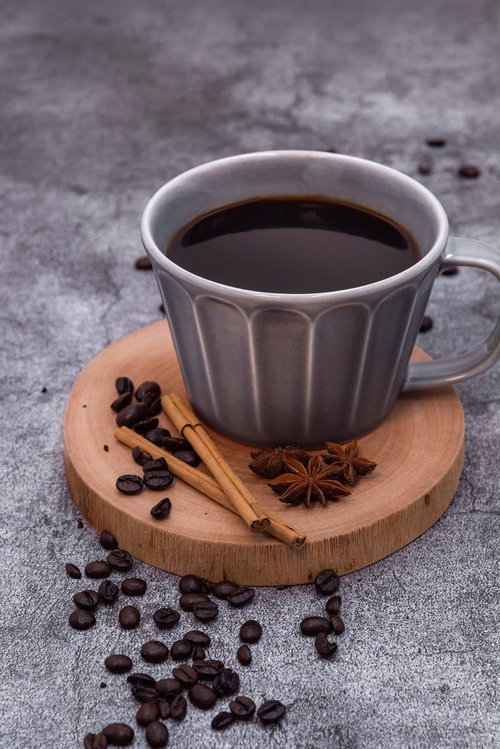 散らばったコーヒー豆とシナモン、木製コースターの珈琲