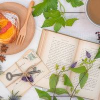 白い背景に広げた洋書とフルーツデニッシュ、コーヒーとともに飾られた植物の写真