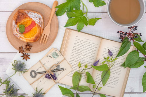 白い背景に広げた洋書とフルーツデニッシュ、コーヒーとともに飾られた植物