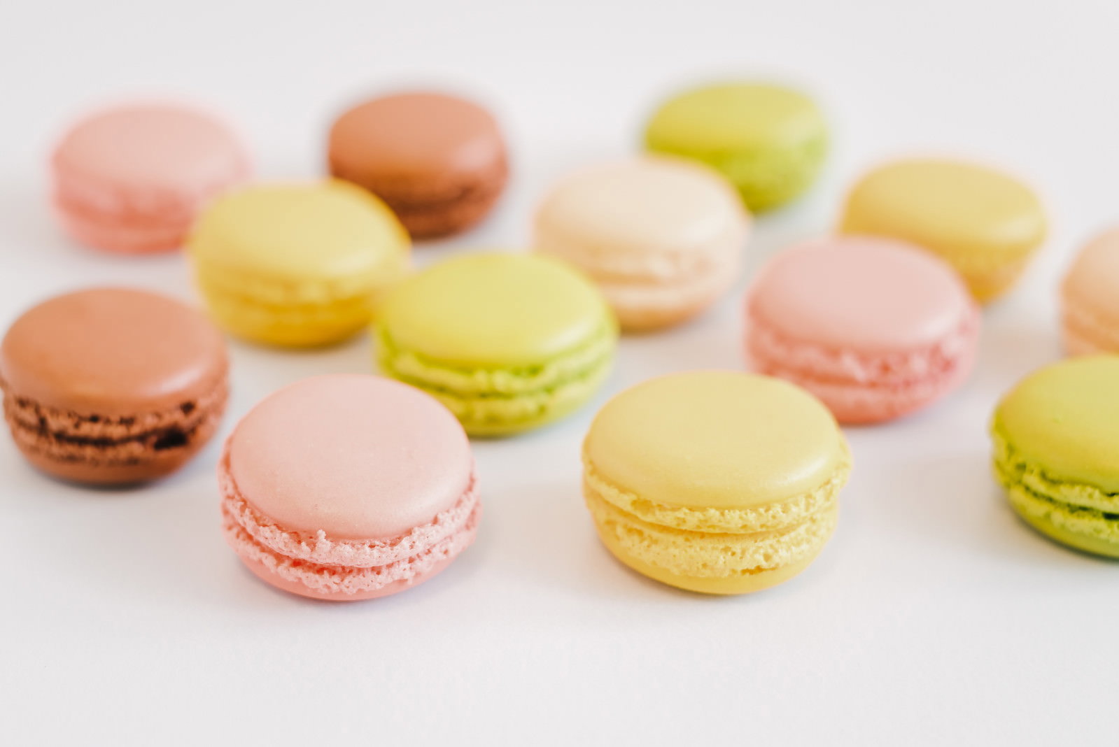 白い背景にピンクやイエロー、グリーンなど色とりどりのマカロンが散らばって配置されている
