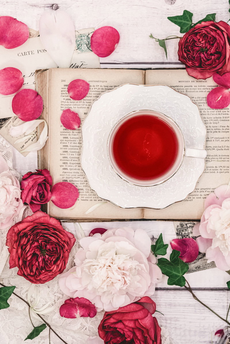 白い木製テーブルに置かれたローズティーのカップと散らばる薔薇の花弁
