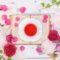 白いカップに入ったローズティーを囲むピンクのバラの花びらの写真