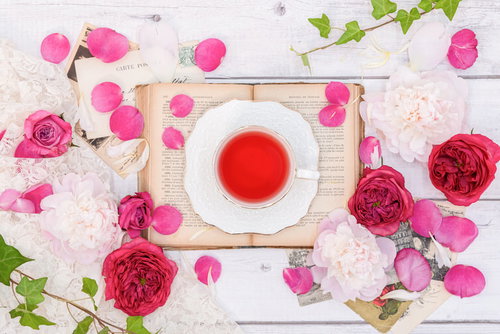 白いカップに入ったローズティーを囲むピンクのバラの花びら